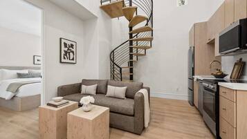 Un apartamento moderno con una escalera espiral, un sofá, una pequeña mesa de madera y una kitchenette.
