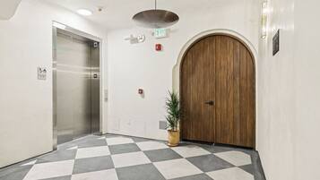 Un pasillo con piso de tablones, una puerta de madera, un ascensor y una planta en maceta.