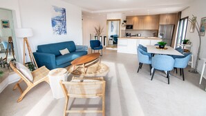 Ein modernes Wohnzimmer mit einer Couch, einem Couchtisch und Sesseln, ein Essbereich mit Tisch und Stühlen sowie eine Küche mit Schränken und Geräten.
