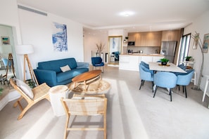 Ein modernes Wohnzimmer mit einer Couch, einem Couchtisch und Sesseln, ein Essbereich mit Tisch und Stühlen sowie eine Küche mit Schränken und Geräten.