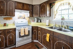 Una cocina con armarios de madera, estufa, lavaplatos y una ventana con cortinas florales.