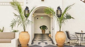 A checkered floor, a sofa, two large planters, a table with chairs, and a doorway with an exit sign. - Casa Iglesia Studio 204 (Santa Barbara)