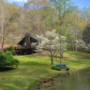 Eine Hütte mit Terrasse, umgeben von Bäumen und einem Teich.