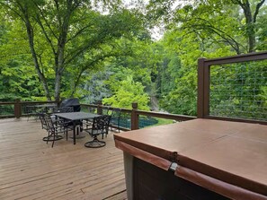 Eine Holzterrasse mit Gartenmöbeln, einem Grill und Blick auf ein bewaldetes Gebiet.