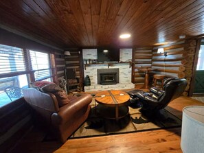 Ein Blockhaus-Interieur mit Kamin, Ledersofa und einem runden Holztisch.