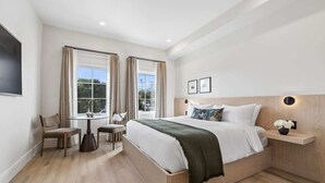 A modern hotel room with a large bed, a small table, two chairs, a TV, and a window with curtains. - Casa Iglesia Studio 202 (Santa Barbara)