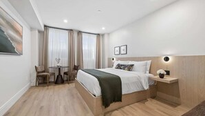 A modern hotel room with a bed, a small table, two chairs, a nightstand, and a wall-mounted light. - Casa Iglesia Studio 106 (Santa Barbara)