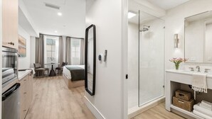 Een moderne hotelkamer met kitchenette, een eethoek, een grote spiegel, een douche en een badkamer met wastafel.