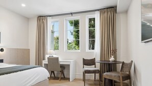 A bedroom with a bed, desk, two chairs, a small table, and a TV. - Casa Iglesia Studio 113 (Santa Barbara)