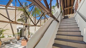Una escalera conduce a un nivel superior, rodeada de un suelo a cuadros, con una palmera y un sofá en primer plano.
