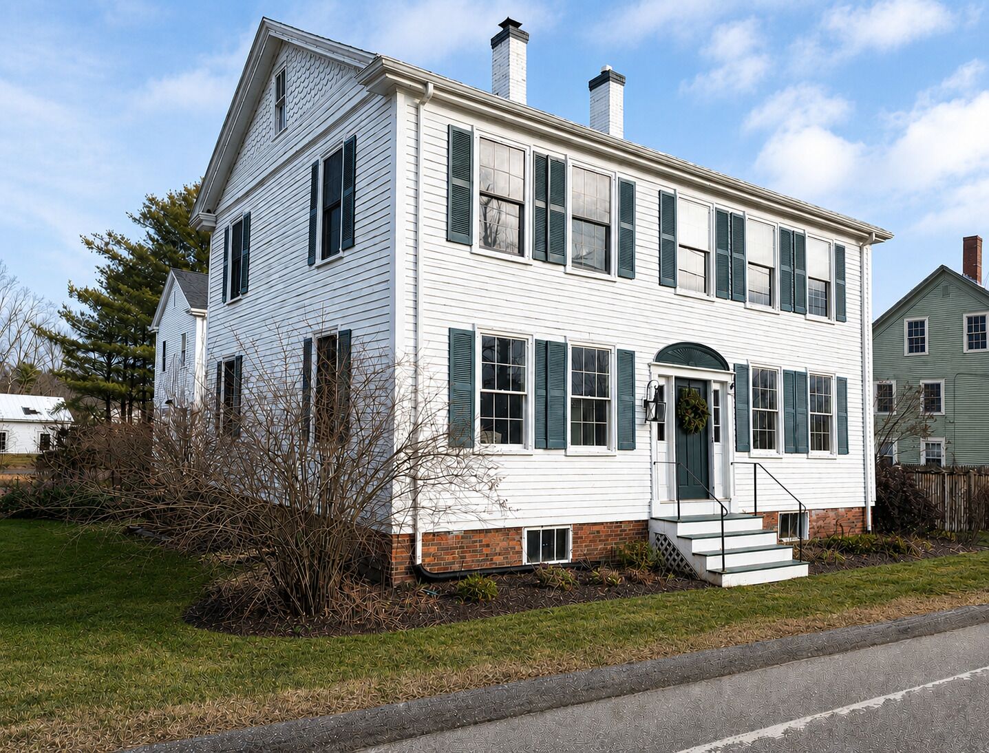 A two-story white house with a brick foundation, green shutters, and a front porch.