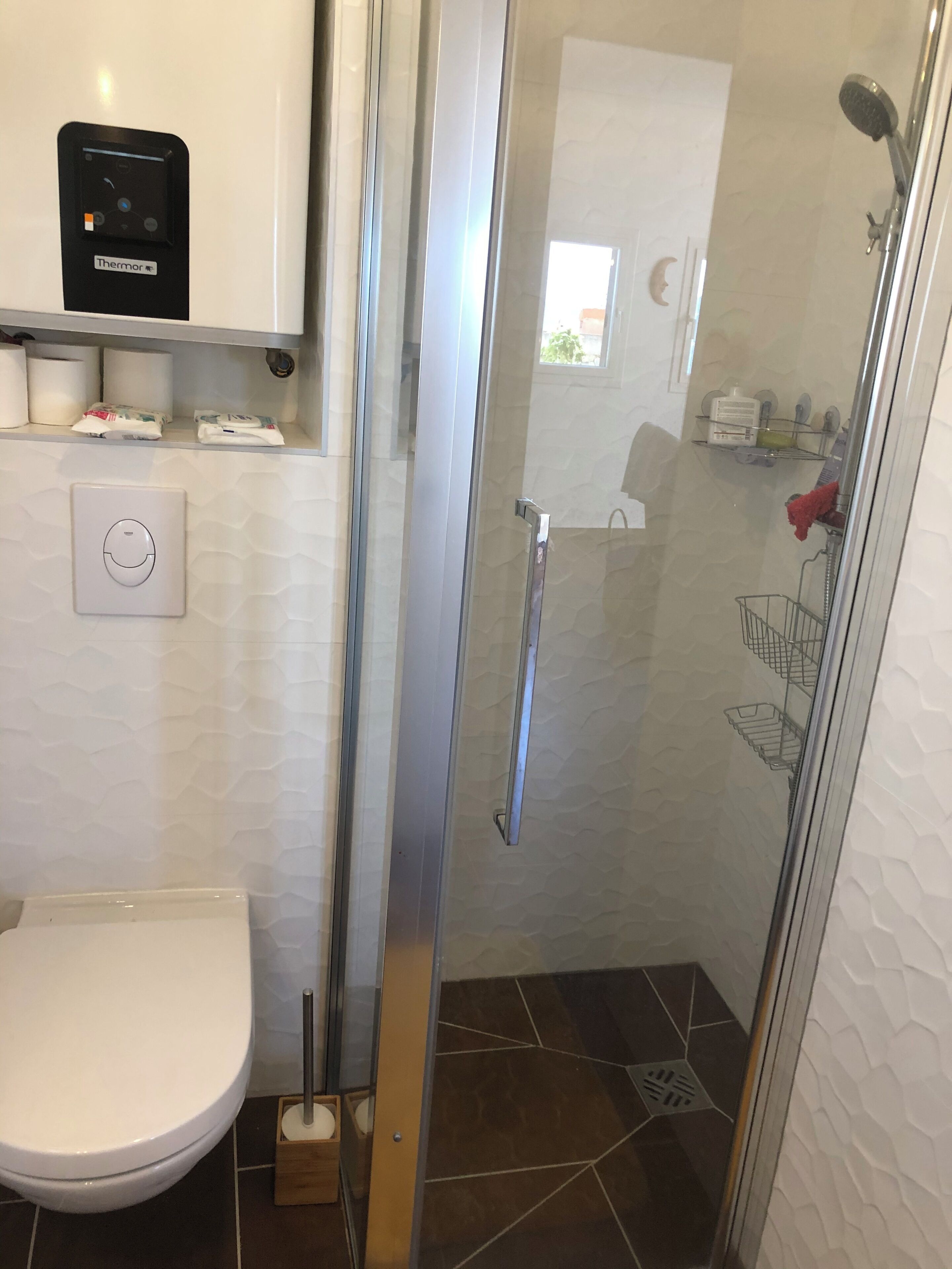A bathroom with a toilet, a shower, a glass door, and a control panel.