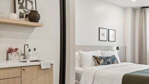 Et moderne hotelværelse med et træskab, en vask, en seng med hvide sengetæger og to billeder hængende på væggen.