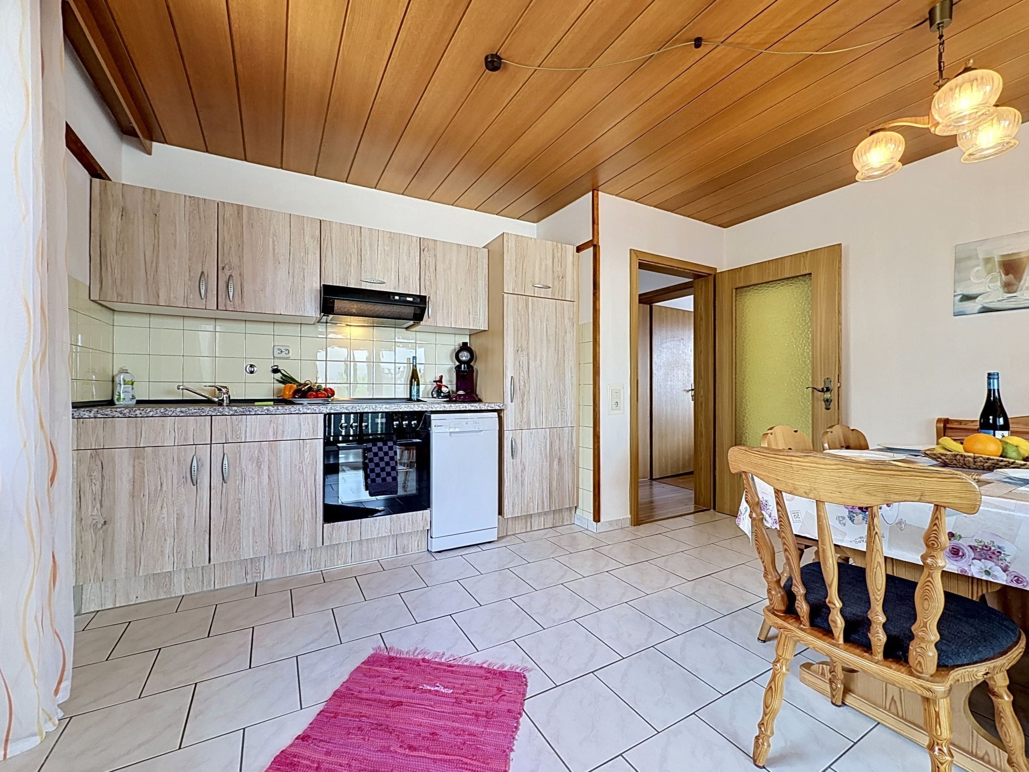 Una cocina con armarios de madera, lavavajillas y un comedor con mesa y sillas.