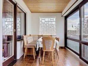 Een eetruimte met een houten tafel en stoelen, een raam met een patroon en uitzicht op de lucht.