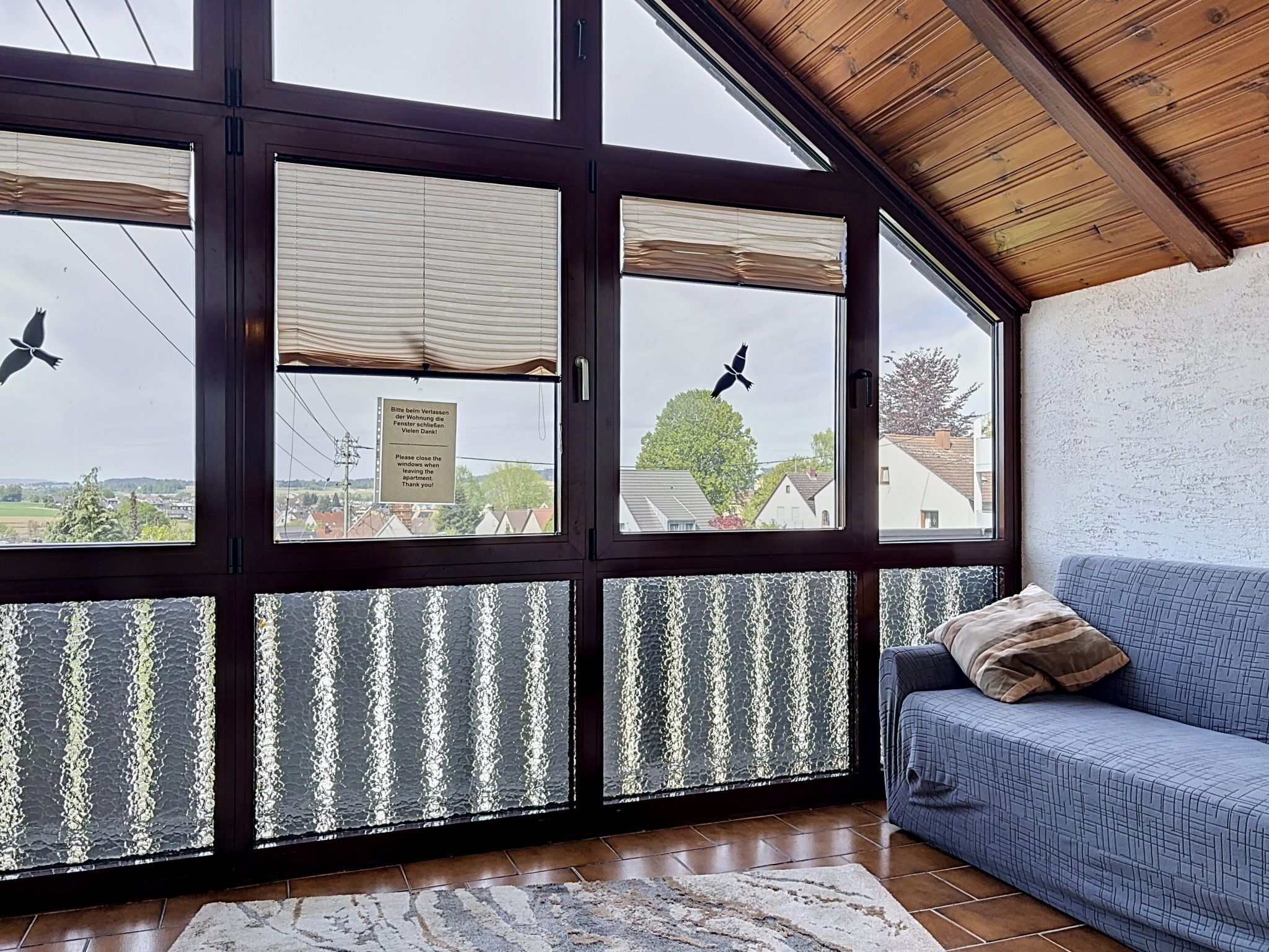 Ein Zimmer mit einem großen Fenster, einem blauen Sofa und einem gemusterten Teppich.