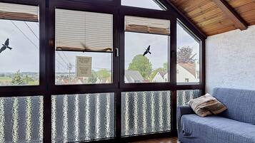 Ein Zimmer mit einem großen Fenster, einem blauen Sofa und einem gemusterten Teppich.