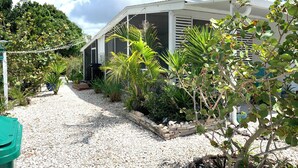 A house with a gravel driveway, surrounded by various plants and trees. - Serene- pool house with large enclosed oasis of local artist in Port Charlotte (Port Charlotte)