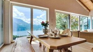 Comedor con mesa de madera, sillas y vista a un lago y montañas.