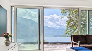 Una sala de estar moderna con un amplio ventanal corredera que da a un balcón con vista al lago.