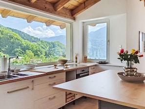 A kitchen with a large window, wooden ceiling, and a view of a mountainous landscape.