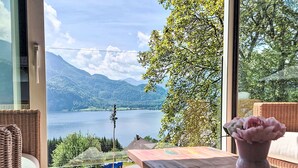 Una habitación con vistas a un lago, montañas y una silla de mimbre.
