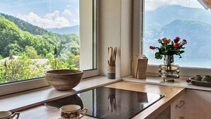 Una habitación con vistas a un paisaje montañoso, una mesa con un cuenco, una taza y un florero con flores.