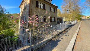 Kaksikerroksinen rakennus, jossa on parveke, aita ja kukkivia puita.