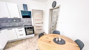 Moderni keittiö, jossa on valkoiset kaapit, sisäänrakennettu uuni ja puinen ruokapöytä tuoleineen.