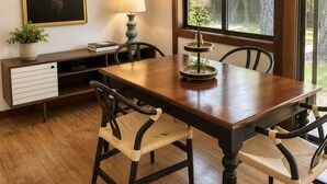 A dining area with a wooden table, chairs, a lamp, a plant, and a framed deer head on the wall.