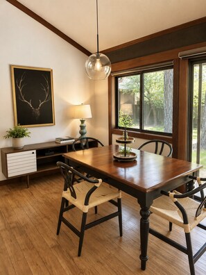 Un comedor con una mesa de madera, sillas, una lámpara, una planta y una cornamenta de venado enmarcada en la pared.