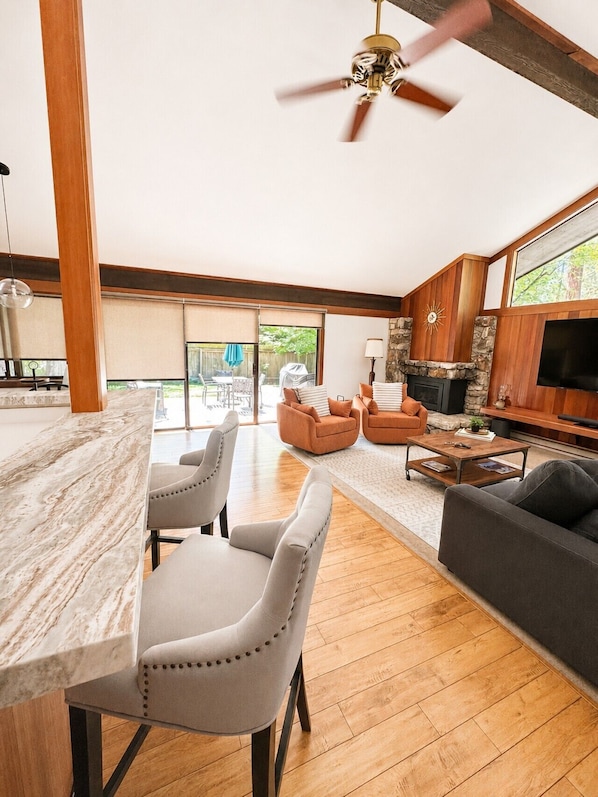 Amplia sala de estar con isla de cocina de mármol, ventilador de techo, chimenea de piedra y televisor grande.