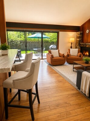 Una sala de estar moderna con chimenea, un comedor con mesa y sillas, y un amplio ventanal corredero que da a un jardín trasero.