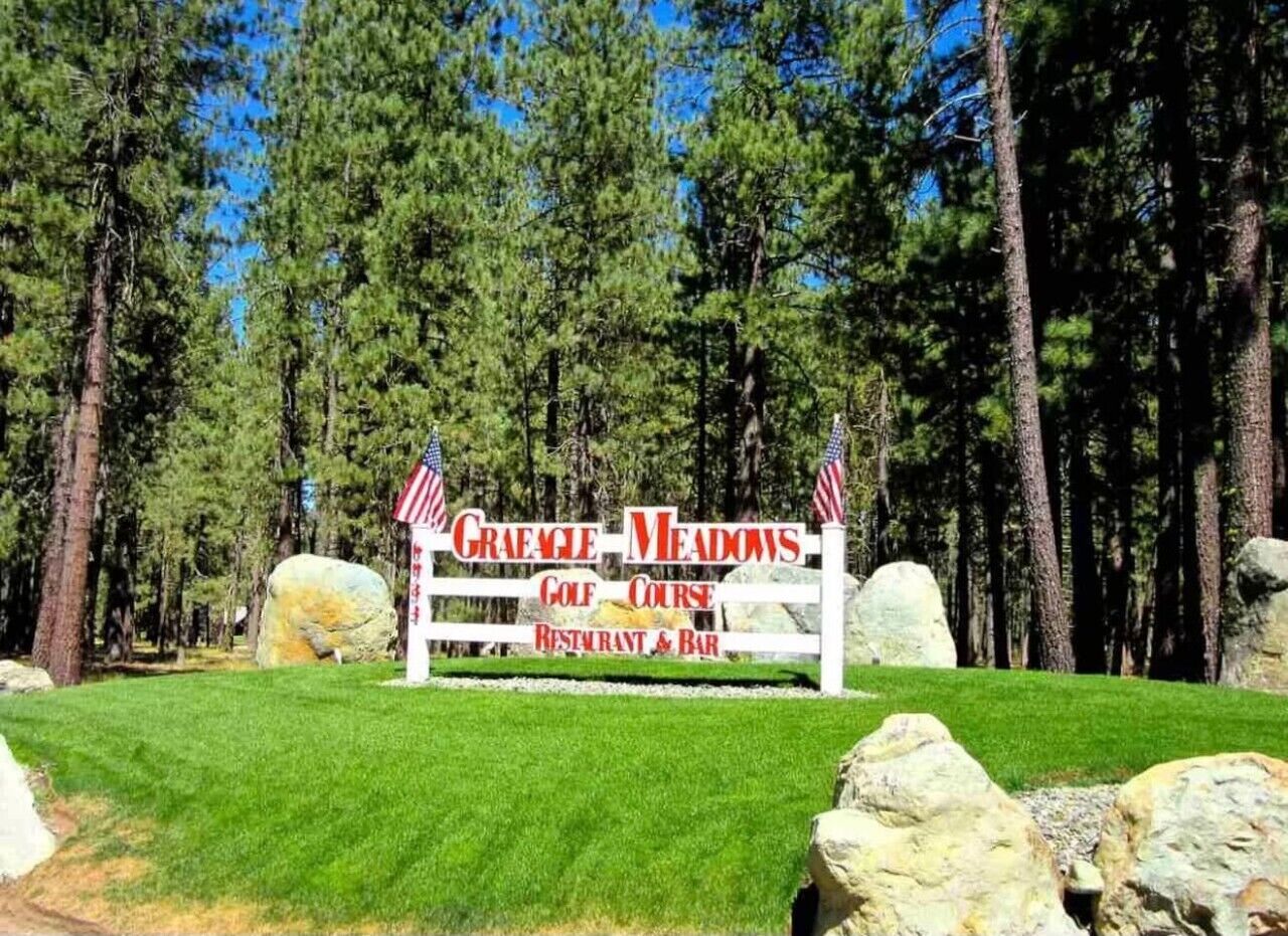 A sign for Graeme Meadows Golf Course Restaurant & Bar surrounded by a forest.