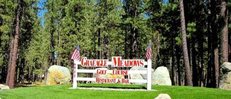 A sign for Graeme Meadows Golf Course Restaurant & Bar surrounded by a forest.