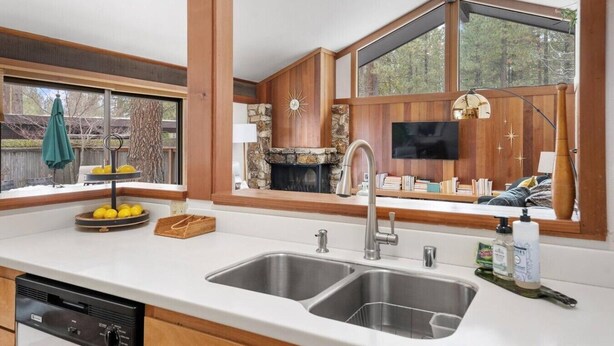 A kitchen with a double sink, a stone fireplace, and a large window overlooking a deck.