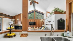 A modern kitchen with a large window, wooden beams, a built-in TV, and a sink.