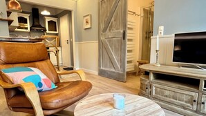 Ein Wohnzimmer mit braunem Ledersessel, einem runden Holztisch, einem Fernseher und einer rustikalen Holzkommode.