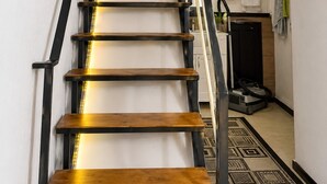 Una escalera de madera con barandales negros que conduce a una plataforma con una lámpara en el techo.