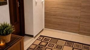 Un pasillo con puerta de madera, una lámpara de pared y un tapete estampado.