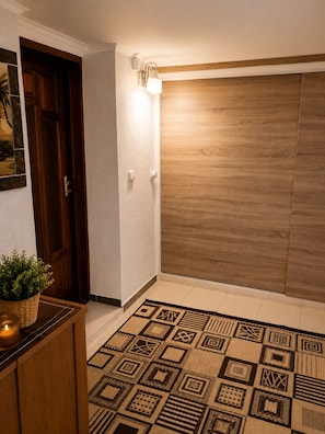 Un pasillo con puerta de madera, una lámpara de pared y un tapete estampado.