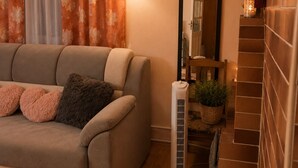 Una sala de estar con un sofá, un calentador portátil, un espejo y una pared de ladrillo.