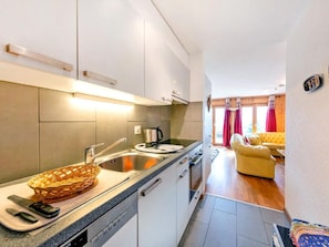 A modern kitchen with a sink, stove, and a dining area with a yellow sofa. - Chalet Arnica by Interhome (Thyon-Les Collons)