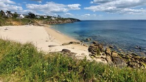 Een kuststrand met heldere lucht, een rotsachtige kustlijn en huizen op de achtergrond.