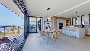 Een moderne keuken met een centraal eiland, een zithoek met rieten stoelen en een balkon met uitzicht.