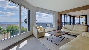 Een ruime woonkamer met grote ramen, een bank, een salontafel en uitzicht op de zee.