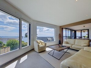 A spacious living room with large windows, a sofa, a coffee table, and a view of the sea. - 4 Mouettes by Interhome (Locmaria-Plouzané)
