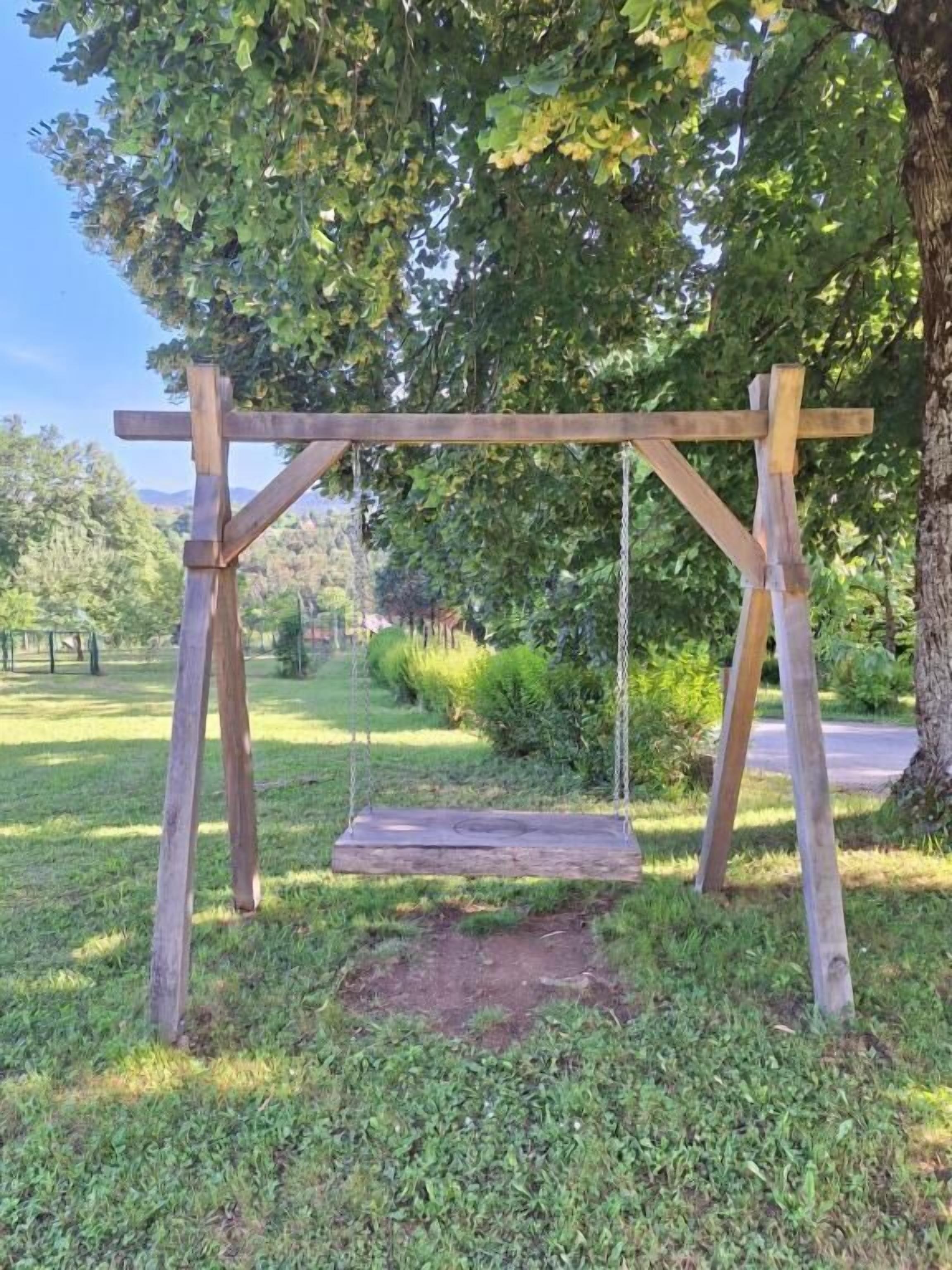 A wooden swing set in a grassy area with trees in the background.