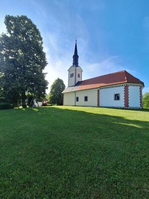 A church with a tall steeple, a red roof, and a white facade. - Mežnarija Cerovec (Dolenjske Toplice)