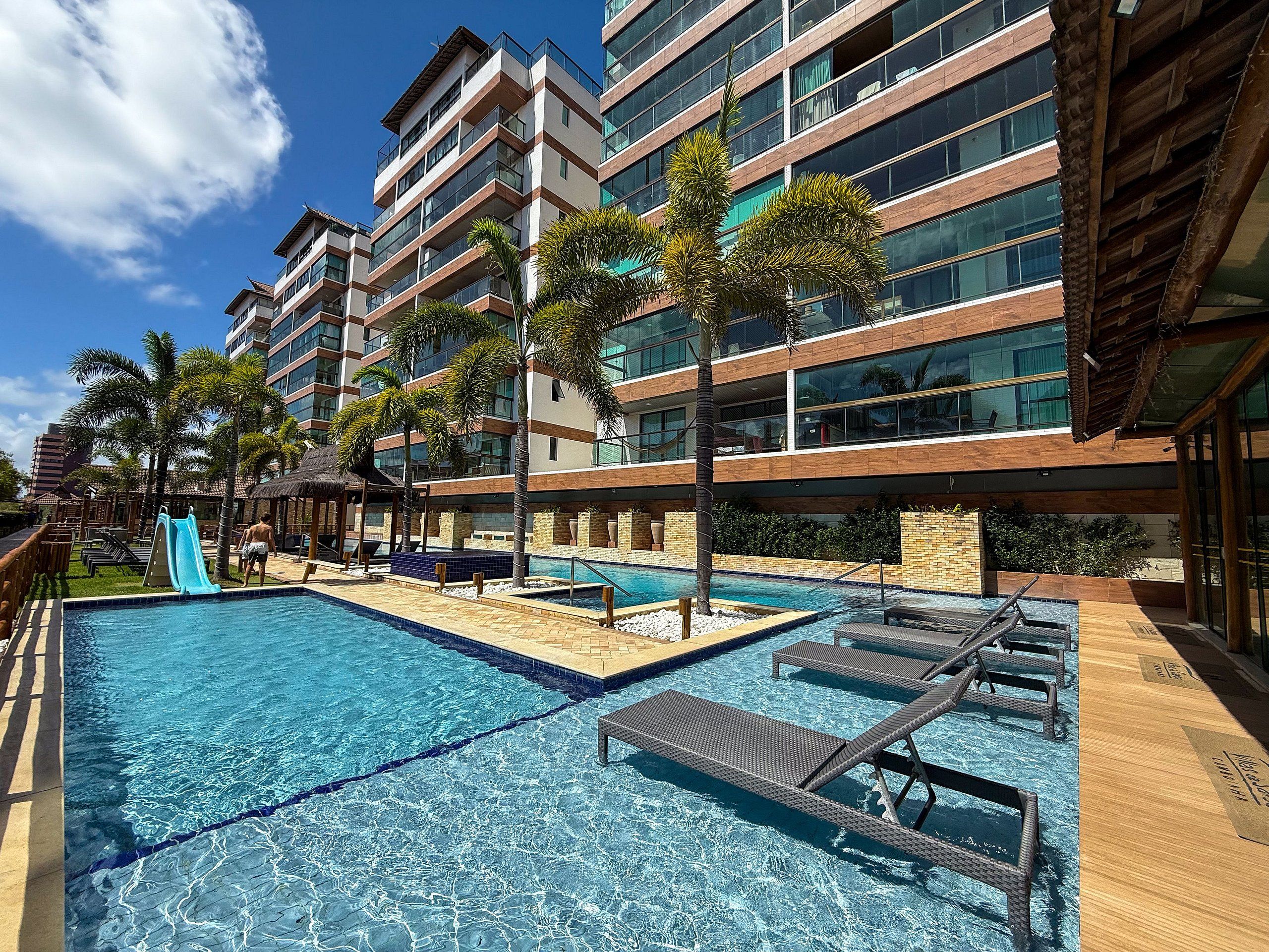 Un espace piscine d’hôtel avec une piscine à l’eau cristalline, des chaises longues et des palmiers.